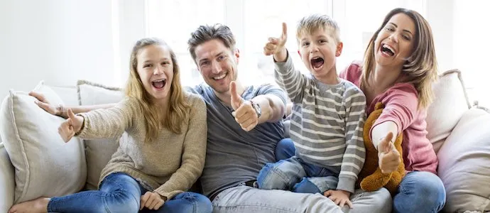 Familie mit zwei Kindern sitzt entspannt auf dem Sofa im eigenen Wohnzimmer